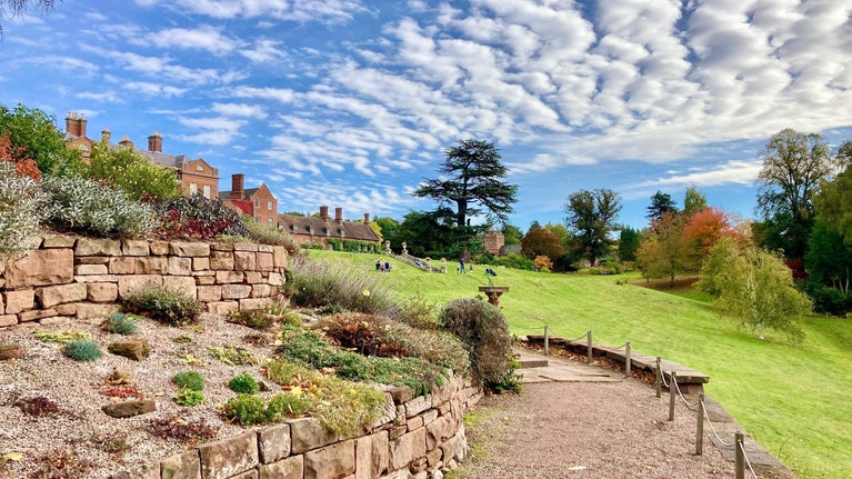 Rockery with alpine plants in front of a red brick stately home and autumnal garden